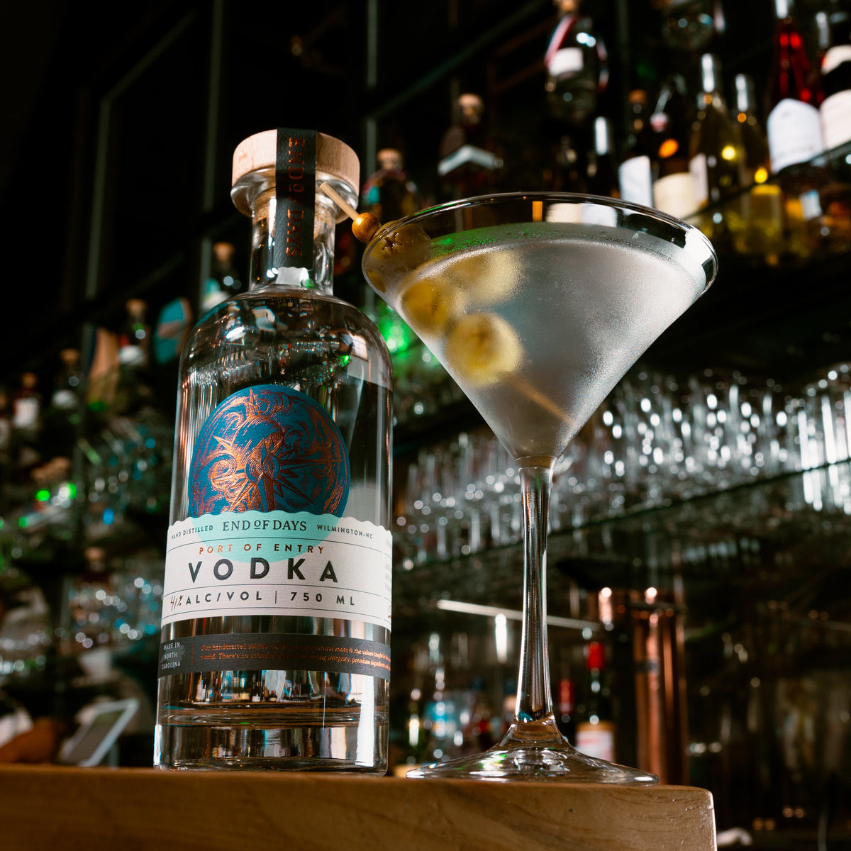 Classic vodka martini with olive beside a bottle of Port of Entry Vodka at the bar